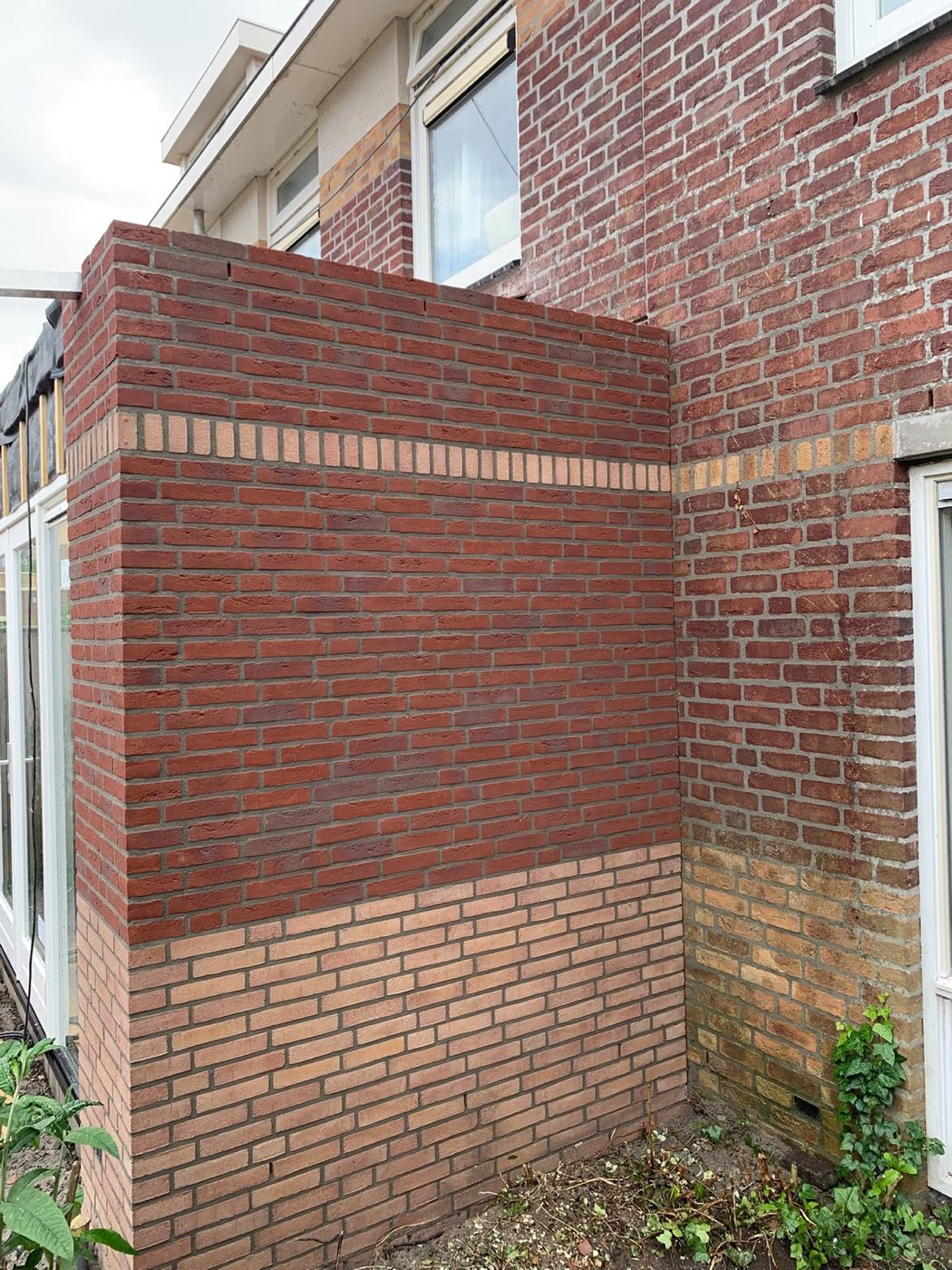 Aanbouw met rode baksteen boven en gele baksteen onder, passend bij het huis