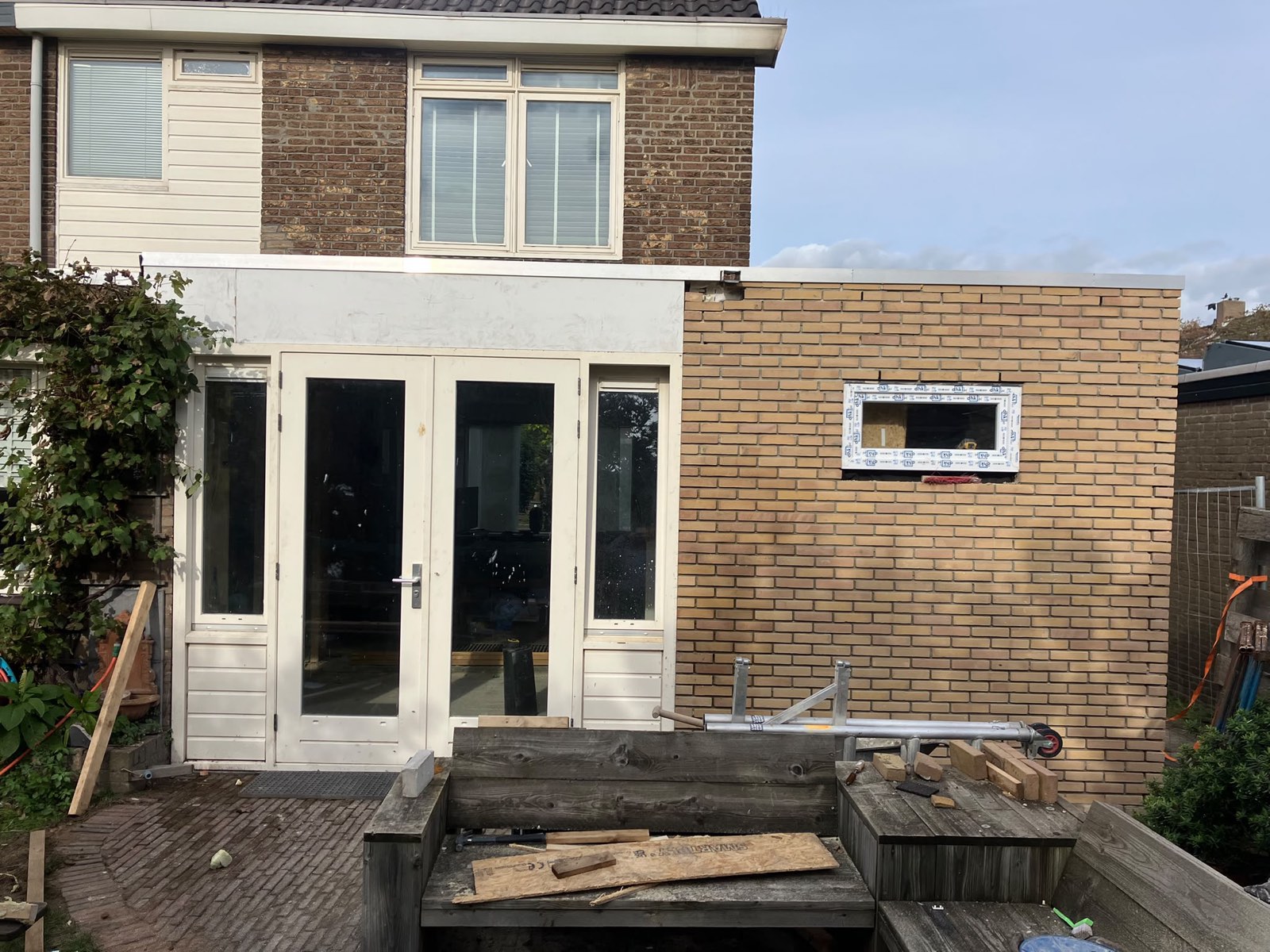 Uitbouw van gele baksteen met witte openslaande deuren